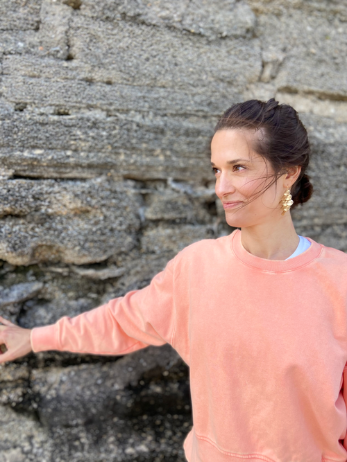 Betsy stands in front of a stone wall, looking to her right with eyes slightly toward the sky and a smile on her face.
