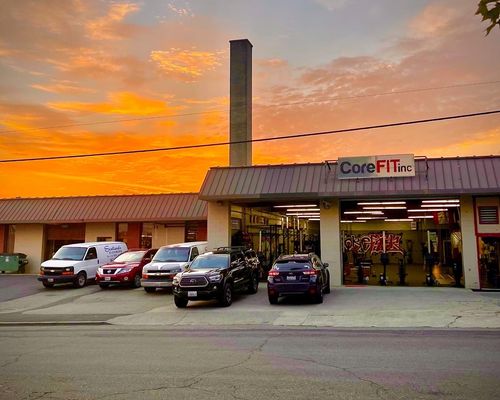 One CoreFit member spots another who is laying on the ground doing overhead presses with a barbell.