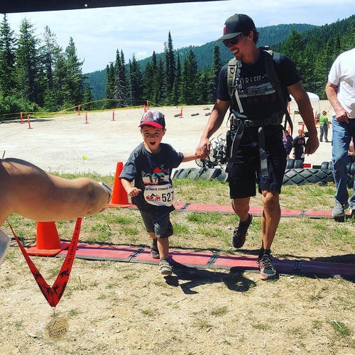 Owner Kurt stands holding hands with his very enthusiastic looking son at an outdoor event.